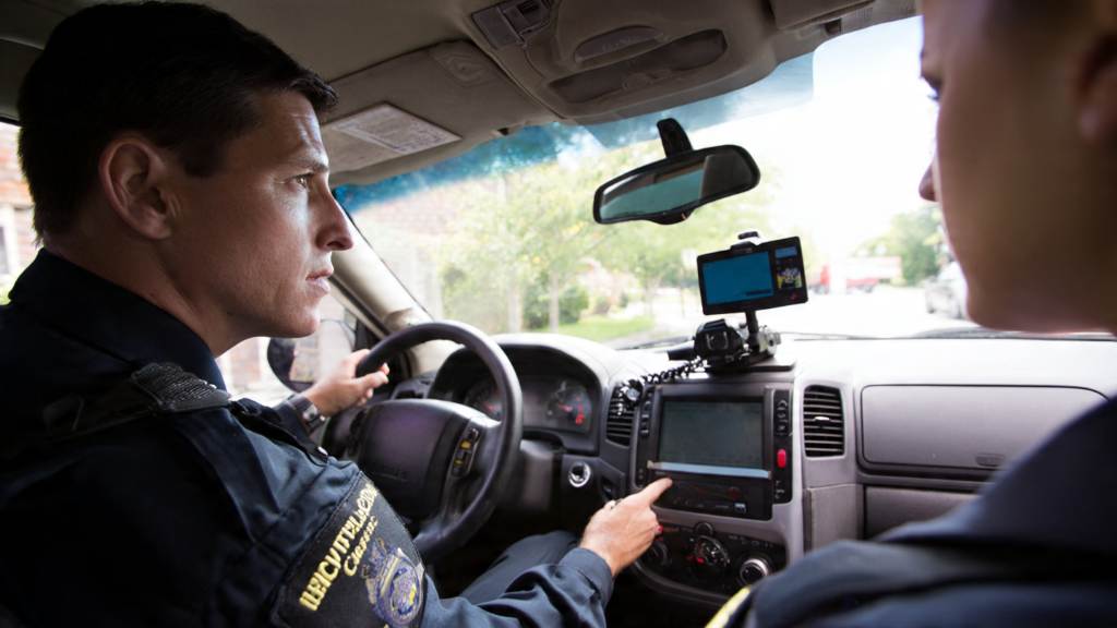 Driver submitting dash cam footage to police officer at station for road incident report.